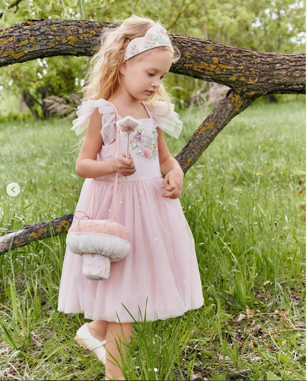 Girl carrying the Whimsy Shroom Bag with a pale pink dress while standing beside a tree by House of Carousél