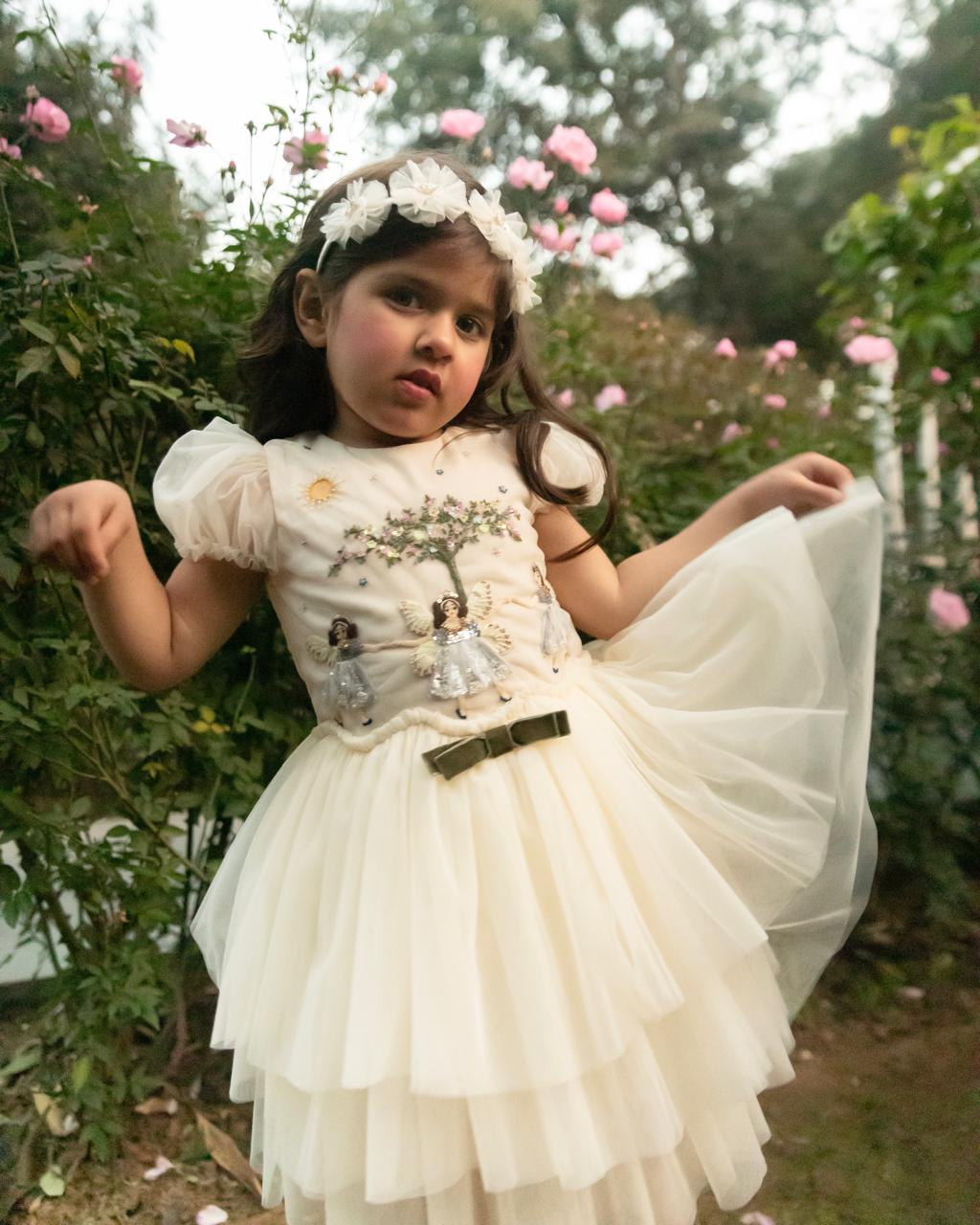 Girl wearing the Three Fairy Friends Dress, an ivory tulle girls’ dress with hand-embroidered fairies and floral details by House of Carousel